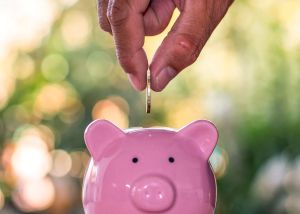 Photograph of a pink piggy bank with someone putting in a coin.