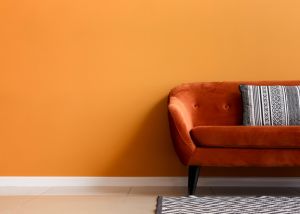 Photograph of a dark orange sofa, against a brighter orange wall with a black and white patterned cushion on it and a black and white patterned rug underneath.