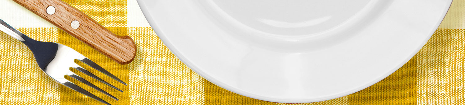 White dinner plate, with knife and fork on a yellow checked table cloth