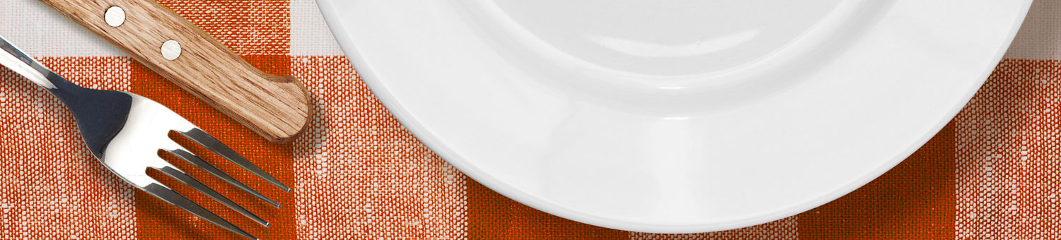 White dinner plate, with knife and fork on a orange checked table cloth